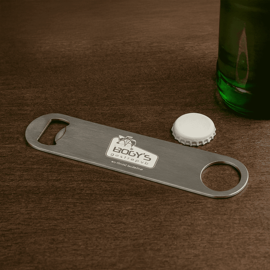 A drink bottle opener in stainless steel with a circular cut-out and a logo, placed near a green bottle and a cap.