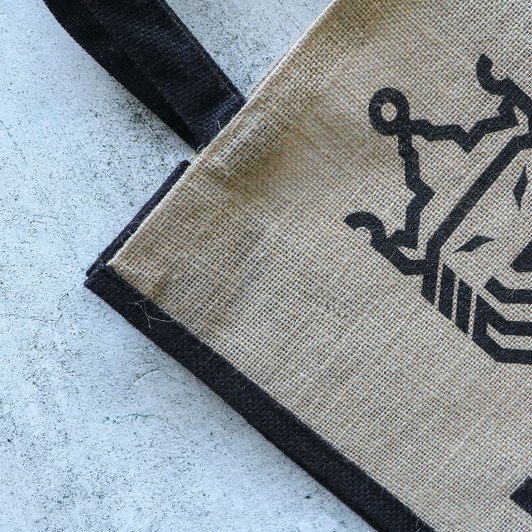A jute tote bag featuring a natural brown body with a black trim and logo.