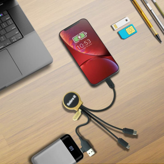 A charging cable in black with multiple connectors, alongside a smartphone and other tech accessories on a wooden desk.