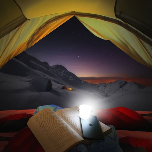 A compact, round white torch illuminating a book, set inside a tent with snowy mountains visible outside.