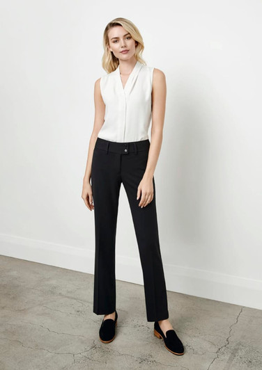 A woman stands in black slacks paired with a white sleeveless top, posed against a neutral background.