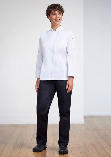 A woman stands wearing a white uniform top and navy scrub bottoms, paired with black shoes, in a bright indoor setting.
