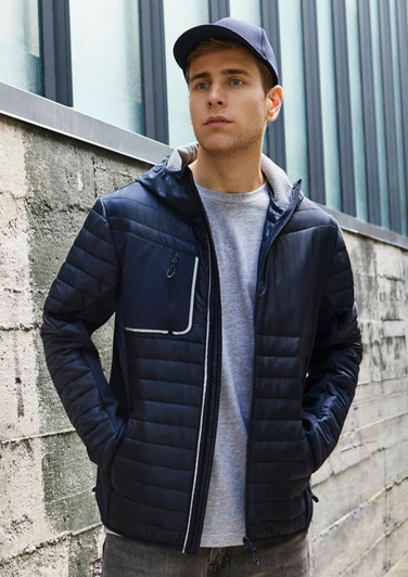 A unisex navy soft shell jacket with a zippered pocket, worn by a model against an industrial backdrop.