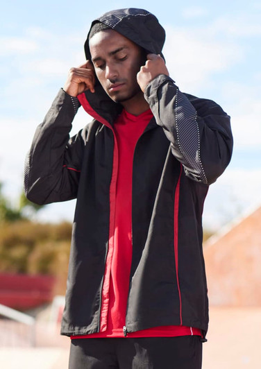 A unisex jacket in black with red accents, featuring a hood and lightweight design, displayed by a model.