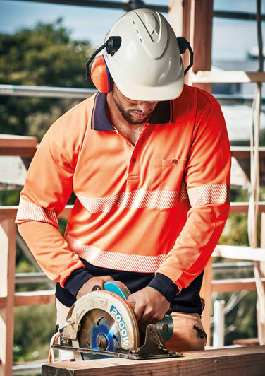A person wearing an orange long sleeve polo shirt with segmented reflective tape operates a circular saw, wearing a helmet and ear protection.