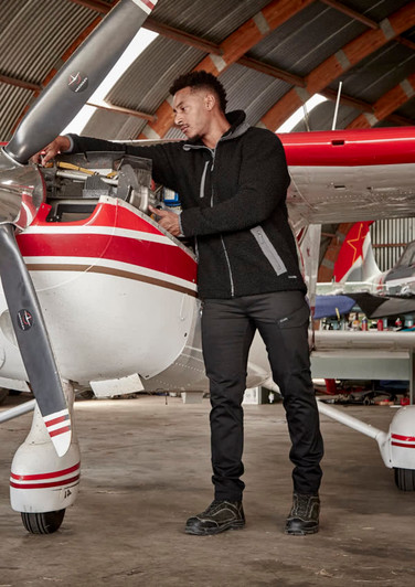 A man wearing a black unisex Sherpa fleece zip jumper, working on an aircraft engine in a hangar.