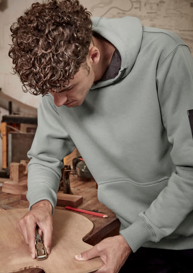 A unisex multi-pocket hoodie in green worn by a person working on wood, featuring a logo on the sleeve.