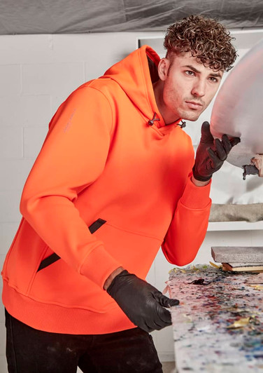 An orange unisex water-resistant hoodie with a black logo, worn by a person in a workshop setting.
