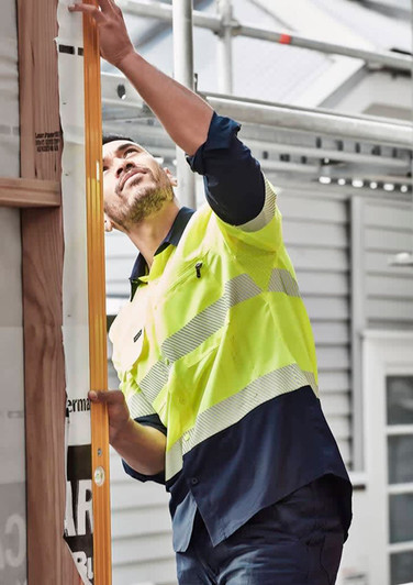 A man wearing a high visibility segmented tape long sleeve shirt in yellow and navy, working on a construction site.