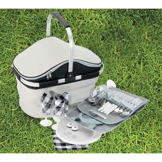 A grey and black picnic carry bag with cutlery, plates, glasses, and salt and pepper shakers on grass.