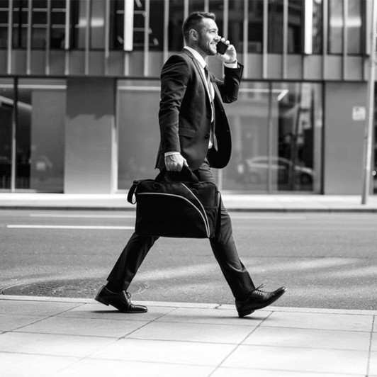 A man in a suit carrying a black conference bag walks confidently on a city street.