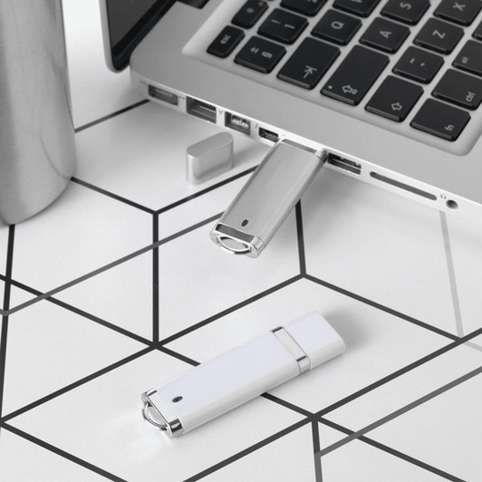 A silver and white USB flash drive is connected to a laptop, with another silver drive nearby on a geometric patterned surface.