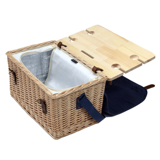 A wicker picnic basket in natural tones, featuring a wooden top with drink holders and a navy blue lining.