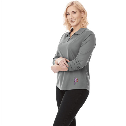 A woman wears a long sleeve grey polo shirt featuring a logo, styled with black pants.