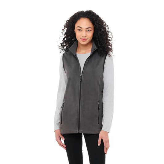A women's polyfleece vest in grey, featuring a zip front and pockets, worn over a long-sleeve top.