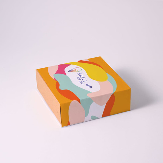 A colorful box with abstract shapes and a logo on top, featuring shades of yellow, orange, pink, and green.