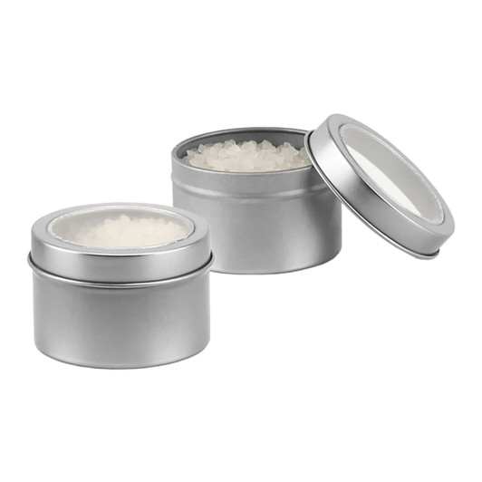 Two silver tin containers filled with white bath salts, one lid partially opened to reveal the contents.