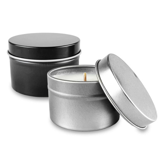 A silver and a black tin candle with lids, featuring a lit wick inside the silver tin.