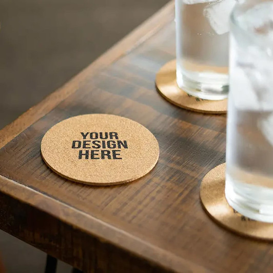 A round cork coaster on a wooden table with two glasses of water and a logo on the coaster.