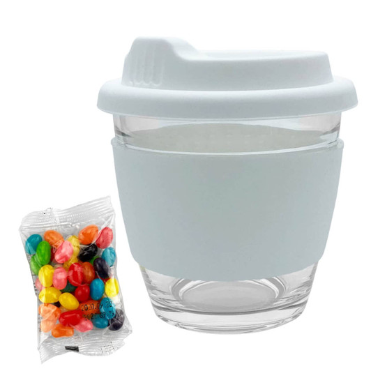 A reusable glass coffee cup in white with a silicone sleeve, alongside a bag of colourful jelly beans.