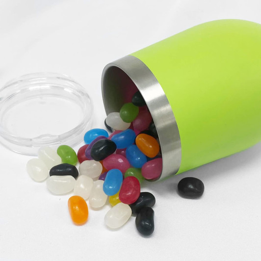 A green coffee mug with a silver rim, filled with colourful jelly beans, tipped over on a white surface.