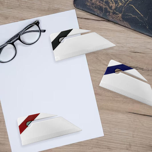 Three white letter openers in black, red, and blue, displayed on a wood surface with glasses and a sheet of paper.