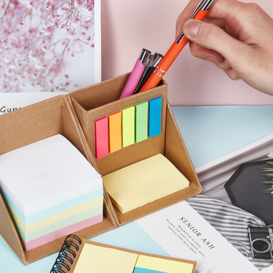 A memo holder in brown cardboard containing sticky notes in pastel and bright colours, with pens inserted.