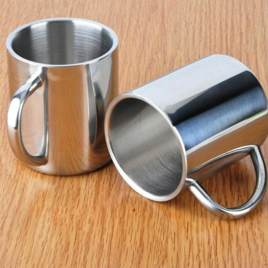 Two stainless steel coffee mugs with smooth surfaces placed on a wooden table. One mug is upright, the other is tilted.
