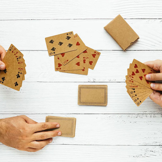 Eco-friendly playing cards in a tan colour, with red and black suits, arranged on a wooden surface with a box.
