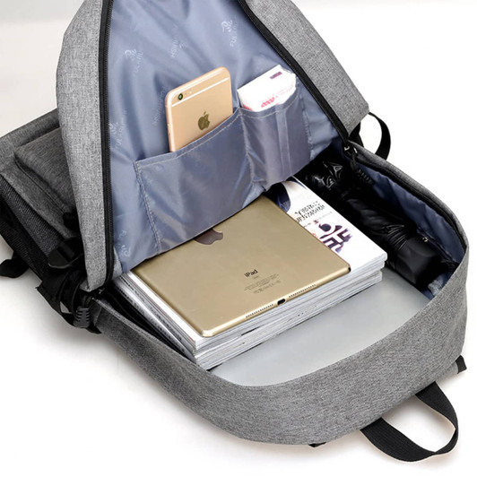 A grey laptop backpack with an open compartment displaying a laptop, magazines, and a mobile phone in pockets.