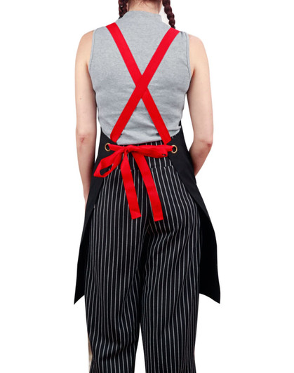 A black canvas bib apron with red straps worn over striped pants, featuring a tied waist and a logo on the back.