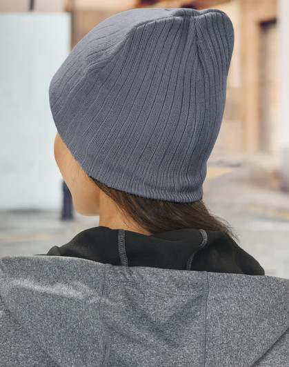 A grey cable knit beanie, viewed from the back, worn by a person in a jacket outdoors.