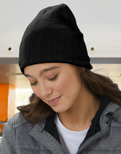 A cable knit beanie in a soft beige colour, worn by a woman with a fleece headband underneath.