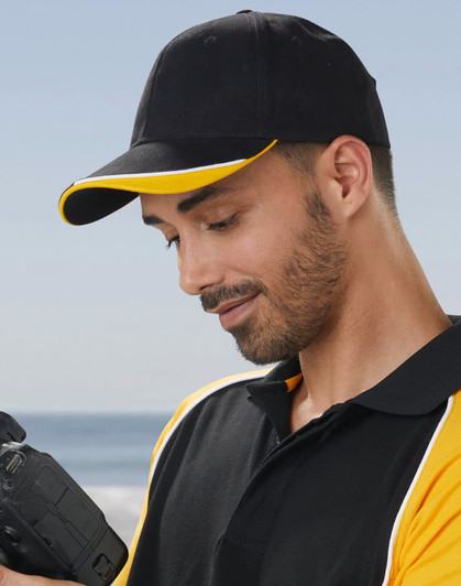 A black cap with a yellow peak, worn by a man holding a camera, featuring a logo on the front.