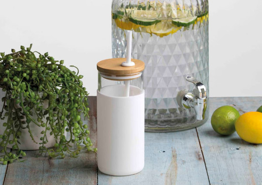 A drink bottle with a white body and bamboo lid, positioned next to a glass dispenser with citrus fruits and greenery.