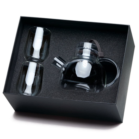 A transparent teapot with two matching cups, all packaged in a sleek black box with textured interior.
