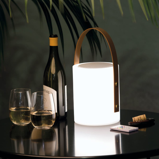 A white speaker lamp with a brown handle, placed beside two glasses of wine and a bottle on a table.