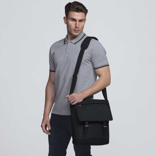 A black messenger bag with adjustable strap, shown on a model wearing a grey polo shirt. The bag has a logo.