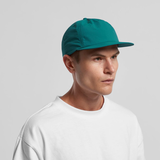 A teal cap with a flat brim, featuring a logo, worn by a male model in a white shirt.