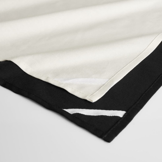 A tea towel featuring a cream top section and a black bottom section, with white stitching details. It has a logo.