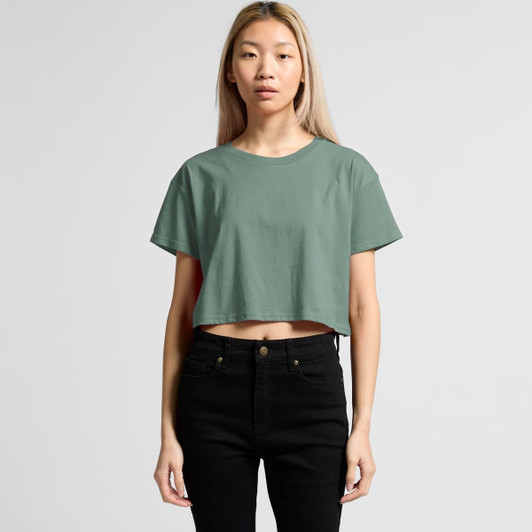 A cropped, green T-shirt with a relaxed fit, paired with black high-waisted jeans. The model stands in a neutral background.