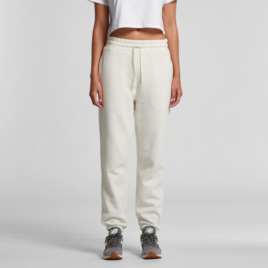 A pair of cream track pants with a drawstring waist and a logo, styled with a cropped top and grey sneakers.