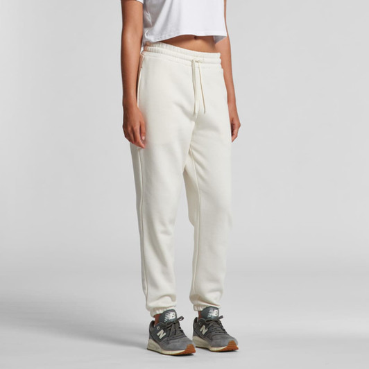 Track pants in cream colour with an elastic waistband and pockets, paired with grey sneakers. Features a logo.