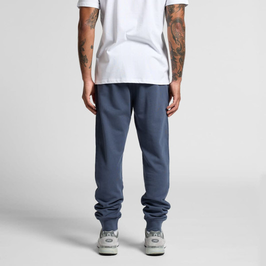 Premium track pants in a dark blue colour, featuring a fitted design and elasticized cuffs. The model is wearing a white shirt.