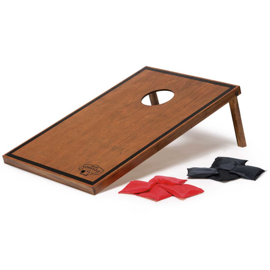 A wooden cornhole board with a hole and four red and four black bean bags. The board features a logo.