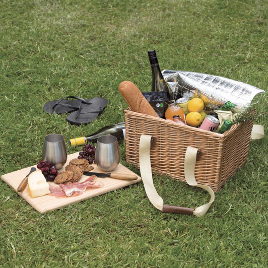 A woven picnic basket filled with drinks, fruits, and snacks, alongside a wooden platter with cheese and meats.
