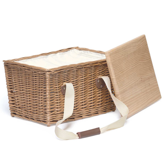 A wicker picnic basket in natural tones with a wooden lid and cream lining, featuring sturdy fabric handles.