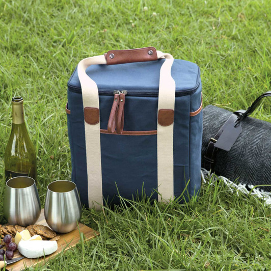 A navy blue wine cooler with a zippered top and light-coloured handles, placed on grass beside wine and snacks.