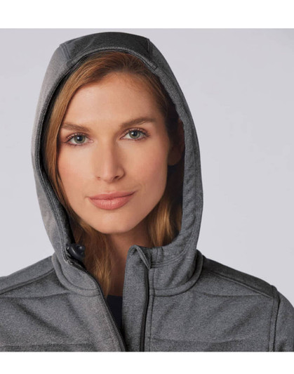A close-up of a woman wearing a grey padded jacket with a hood. The jacket features a logo.