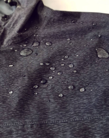 A close-up of a black waterproof performance jacket featuring droplets of water on the surface.
